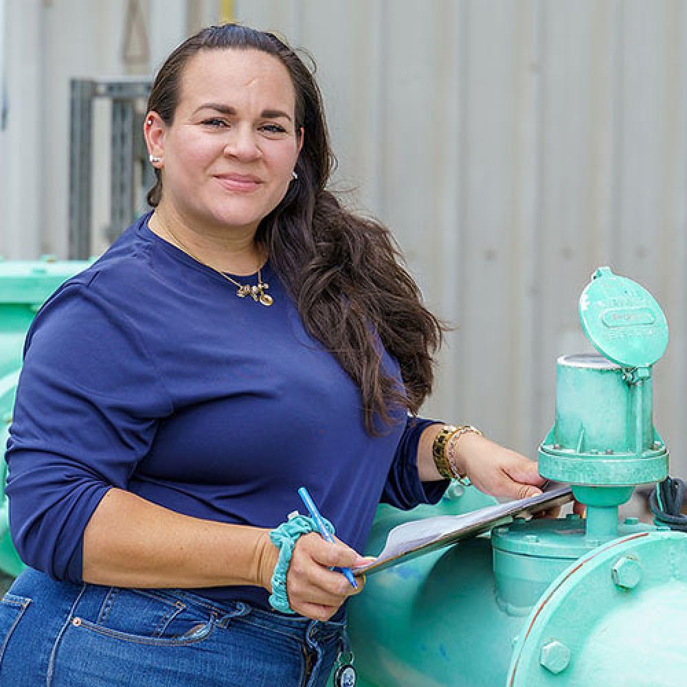 Image of female water plant operator standing at pipe. 