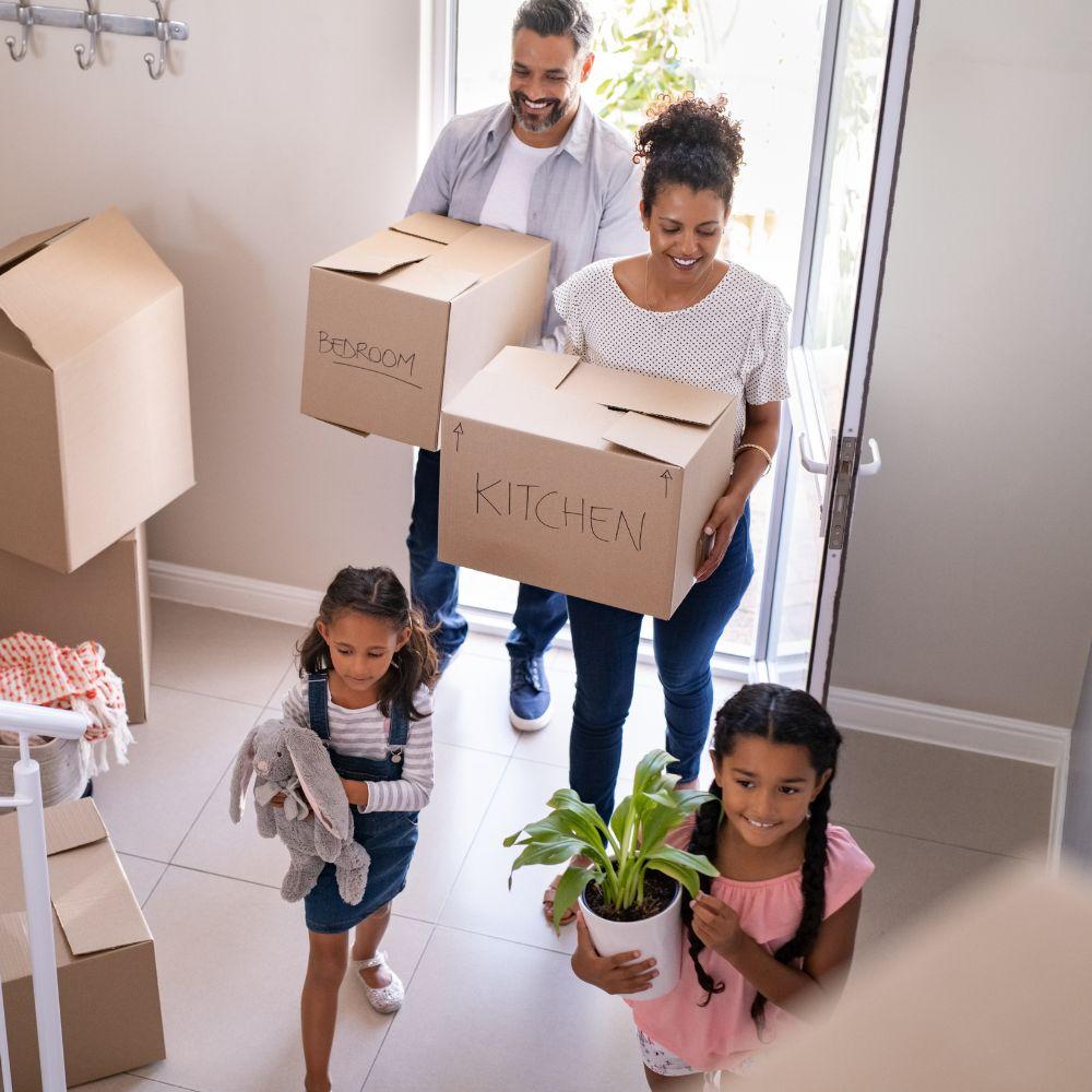 Image shows family carry boxes moving into home. 