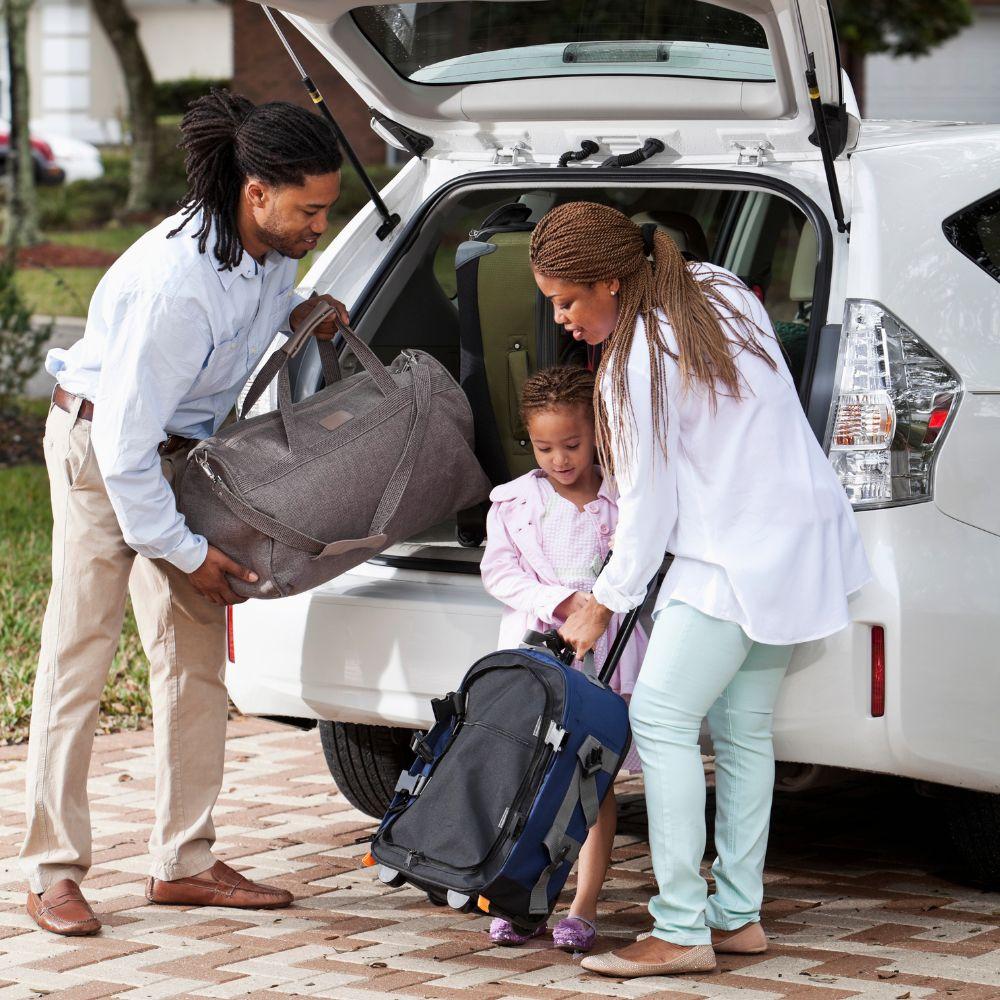 Image shows family putting luggage into the back of a car.