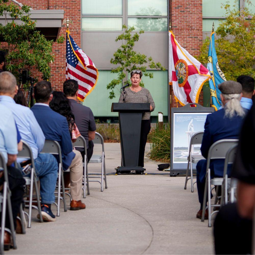 Image of a speaker at a podium addressing a group of people. 