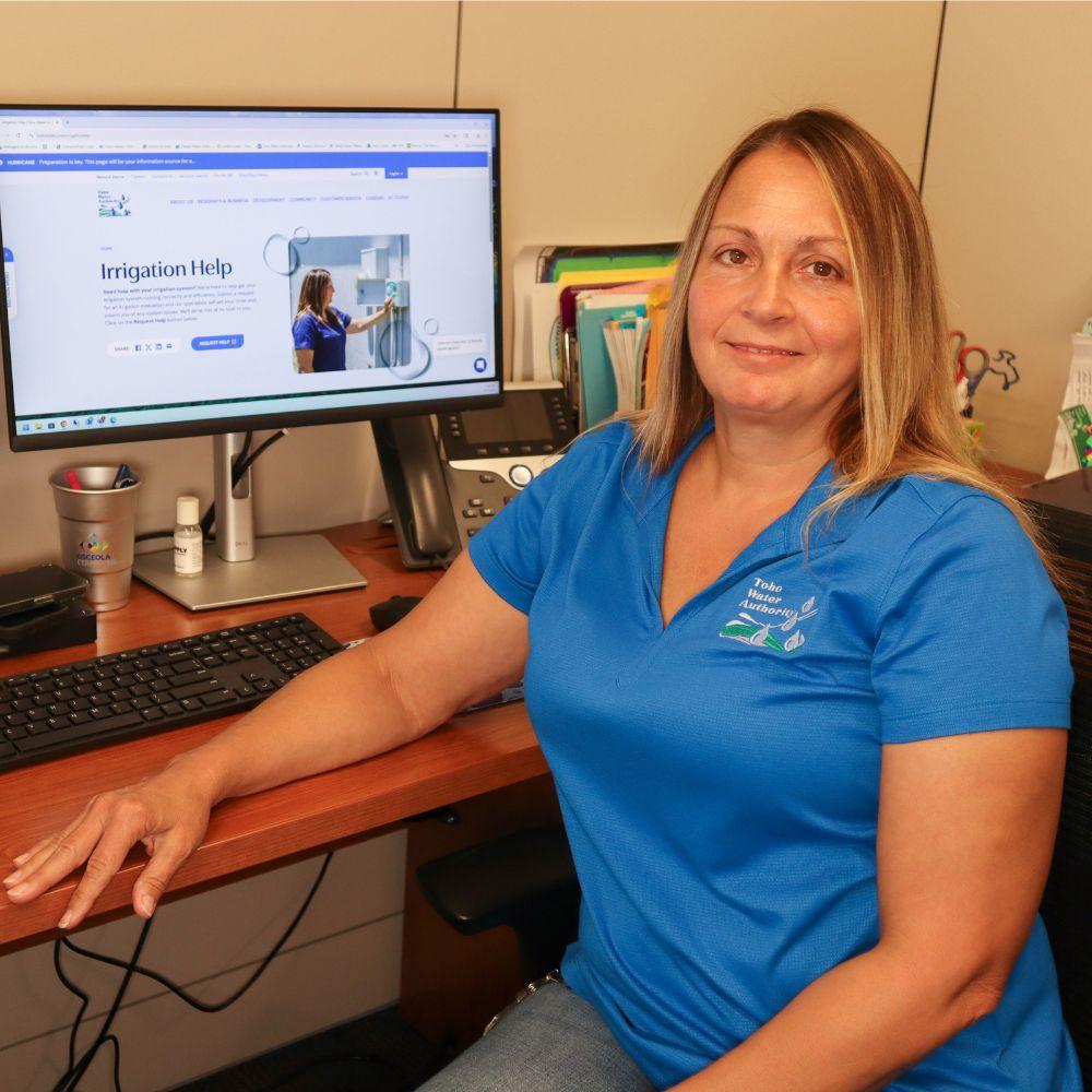 Image of Conservation Specialist at her desk in front of computer smiling at camera. 