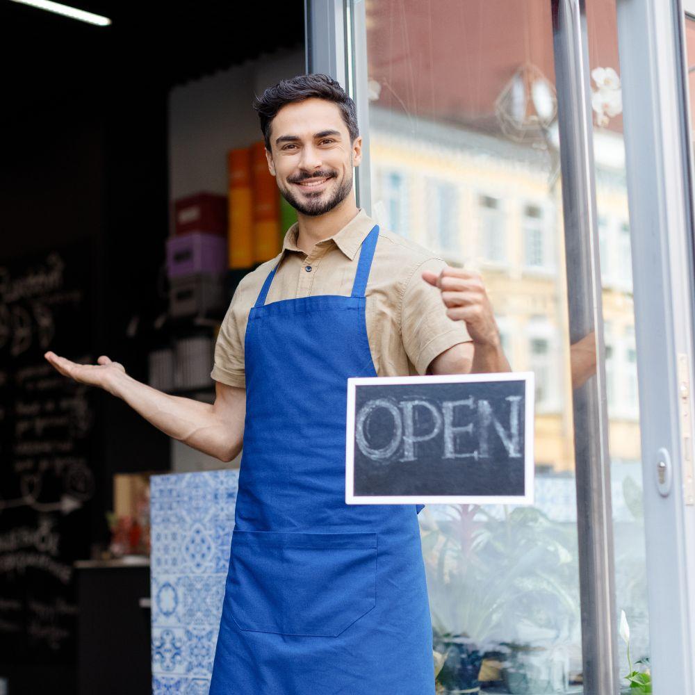 Image of a man standing in business doorway holding an open sign.