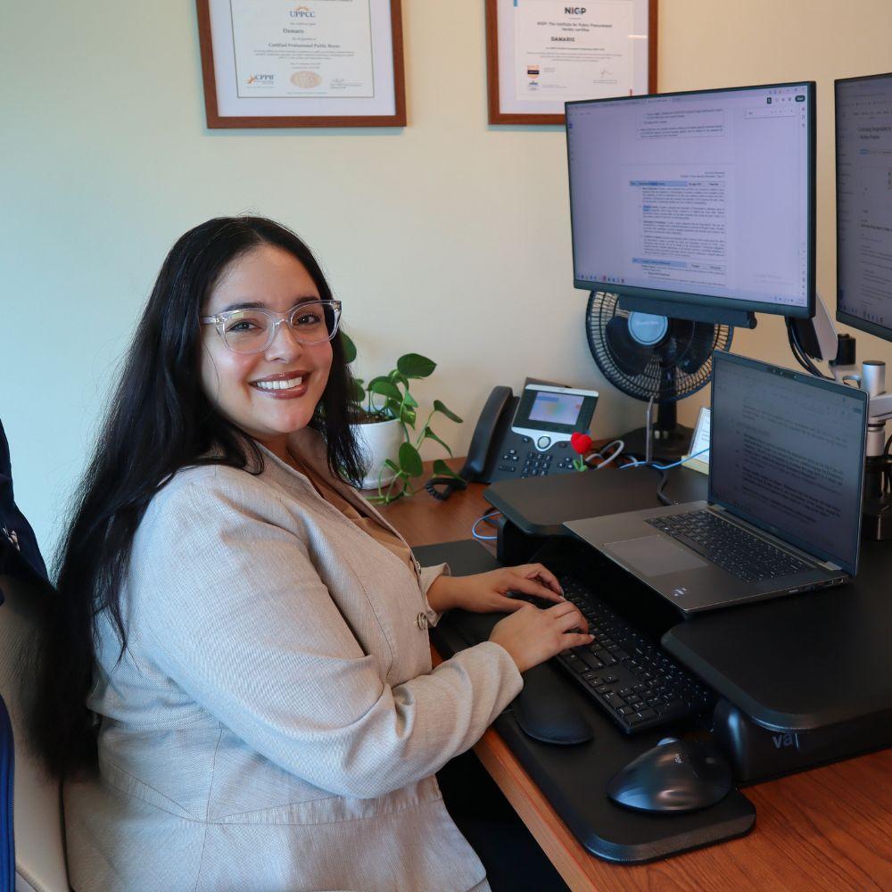 Toho female employee in her office sitting at computer smiling at camera. 