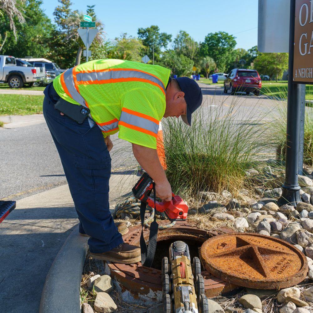 Technician looks into a sewer manhole holding a flashlight. 